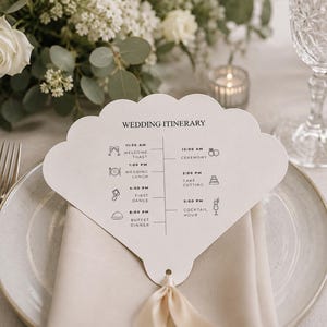 Può includere: Un biglietto dell'itinerario di nozze a forma di ventaglio, con un nastro beige, poggia su un piatto con un tovagliolo piegato. Il biglietto elenca il programma del matrimonio con orari e icone. Un'arrangiamento floreale e bicchieri sono sullo sfondo.