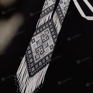 May include: A long, white and black beaded necklace with a geometric pattern. The necklace has a fringe of white beads.