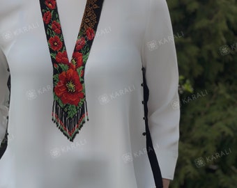 May include: A beaded necklace with a floral design featuring red poppies, green leaves, and black beads. The necklace is long and hangs down to the chest.