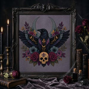 May include: A cross-stitch embroidery featuring a central black raven with spread wings, positioned above a beige human skull. The design includes a crescent moon, deep red roses, and purple floral accents on a gray fabric, encased in a dark frame.