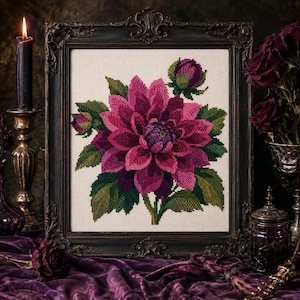 Peut inclure: Une broderie au point de croix représentant un dahlia magenta vif avec des feuilles vertes et deux boutons, présentée dans un cadre rectangulaire orné sombre. L'ouvrage présente des nuances pixélisées sur un fond en tissu beige clair.