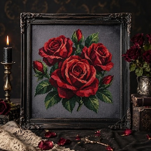 May include: A square cross-stitch embroidery featuring three vibrant red roses and green leaves on a dark gray fabric background, encased in an ornate, dark, weathered wooden frame with intricate carved detailing along the edges.