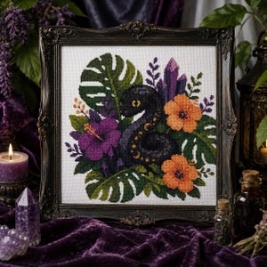 May include: A cross-stitch embroidery in a dark ornate frame featuring a black snake with yellow crescent moon markings, surrounded by green monstera leaves, a large purple hibiscus flower, two orange hibiscus flowers, and purple crystal clusters.