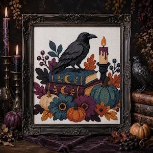 May include: A framed cross-stitch embroidery featuring a black raven perched on two stacked books with gold crescent moon motifs, surrounded by a lit candle, a teal pumpkin, an orange pumpkin, and various autumn-colored flowers and leaves.