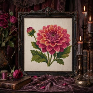 May include: A framed cross-stitch embroidery featuring a large, vibrant pink and orange dahlia flower with a smaller bud and green leaves on a light beige fabric background, enclosed in an ornate, dark brown, vintage-style rectangular frame.