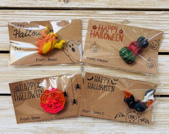 May include: Four Halloween-themed crayon sets in clear packaging. Each set features a unique crayon design, including a ghost, pumpkins, a spider web, and a bat. The cards read "Happy Halloween" and "From:" with a name.