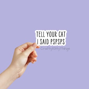 Puede incluir: Pegatina blanca con texto negro que dice "Tell your cat I said pspsps" y el texto "CraftyKittyThings" en una fuente más pequeña debajo.