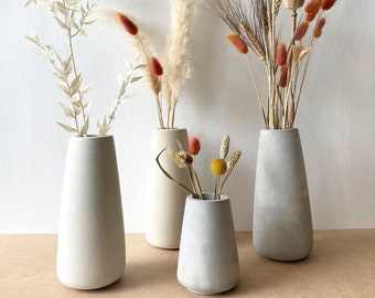 May include: Four concrete vases in different sizes and shades of gray, filled with dried flowers and grasses. The vases have a rounded, tapered shape.