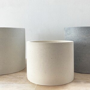 Pode incluir: Tr&ecirc;s vasos de cimento de diferentes tamanhos e cores. O vaso maior &eacute; oval e branco. O vaso m&eacute;dio &eacute; redondo e branco. O vaso menor &eacute; redondo e cinza.
