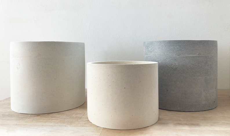Pode incluir: Tr&ecirc;s vasos de cimento de diferentes tamanhos e cores. O vaso maior &eacute; oval e branco. O vaso m&eacute;dio &eacute; redondo e branco. O vaso menor &eacute; redondo e cinza.