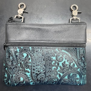 May include: A small black leather bag with a teal paisley pattern. The bag has two silver clips on the top.