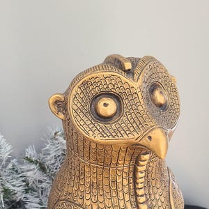 May include: A gold owl statue with intricate details and large, round eyes. The owl is standing on a square base.
