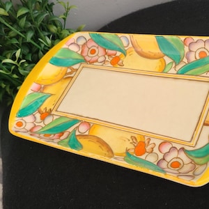 Könnte beinhalten: Ein gelbes Keramik-Serviertablett mit einem Blumendesign mit Zitronen, Blättern und Blumen. Das Tablett hat einen erhöhten Rand und eine rechteckige Form.