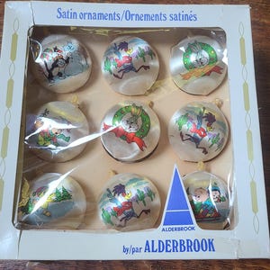 Könnte beinhalten: Ein Set aus neun runden, weißen Satin-Weihnachtskugeln von Alderbrook in einer rechteckigen Schachtel. Jedes Ornament zeigt eine farbenfrohe Looney Tunes-Figur, darunter Bugs Bunny, Road Runner und Sylvester, mit weihnachtlichen Motiven.