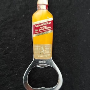May include: A silver bottle opener shaped like a bottle of Johnnie Walker Red Label Scotch Whisky. The bottle opener has a gold label with the Johnnie Walker logo and the words "Red Label Old Scotch Whisky".