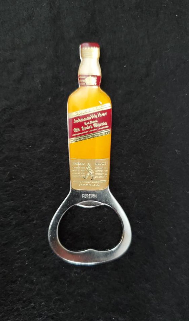 May include: A silver bottle opener shaped like a bottle of Johnnie Walker Red Label Scotch Whisky. The bottle opener has a gold label with the Johnnie Walker logo and the words "Red Label Old Scotch Whisky".