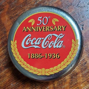 May include: A silver bottle cap with a red and gold design. The cap features the Coca-Cola logo and the text "50th Anniversary 1886-1936".