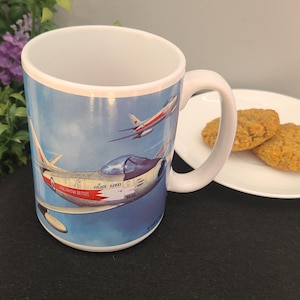 Peut inclure: Mug en céramique blanche avec une illustration détaillée d'avions Golden Hawks canadiens en vol sur fond de ciel bleu. La tasse a une anse et un bord blancs, avec le texte "Golden Hawks" et "Royal Canadian Air Force".