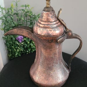 Può includere: Una caffettiera araba vintage in rame e ottone con un coperchio incernierato e un puntale appuntito. La caffettiera ha una patina usurata e invecchiata e disegni incisi intricati.