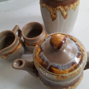 May include: A brown and white ceramic teapot with a lid and a matching creamer and sugar bowl. The teapot has a brown and yellow striped design.