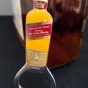 May include: A gold bottle opener with a red and gold Johnnie Walker Red Label Old Scotch Whisky label. The bottle opener has the words "Foreign" and "Avatars" printed on it.