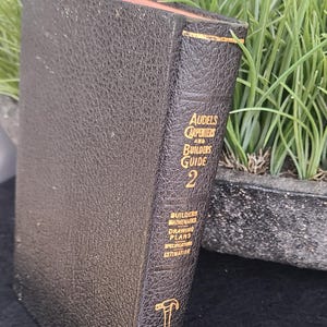 Peut inclure: Un livre relié en cuir noir intitulé "Audels Carpenters and Builders Guide 2". Le livre a des lettres dorées et une petite icône de marteau sur le dos. Le livre porte sur les mathématiques du bâtiment, les plans de dessin, les spécifications et l'estimation.