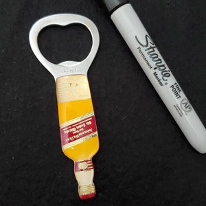 May include: A silver bottle opener shaped like a miniature bottle of Johnnie Walker Red Label Scotch Whisky. The bottle opener has a red label with gold lettering that reads "Johnnie Walker Red Label Old Scotch Whisky" and "Blended Scotch Whisky."
