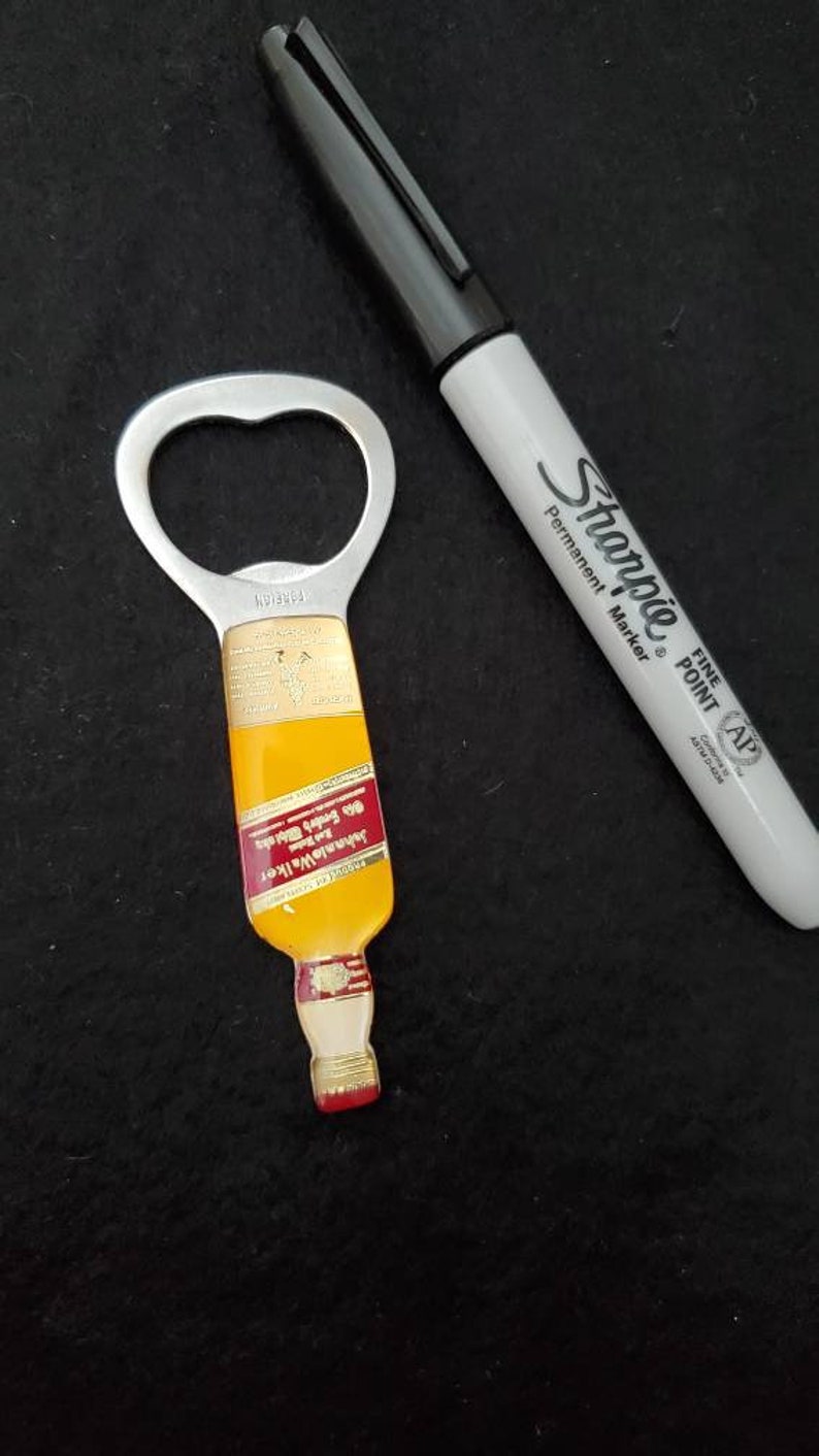 May include: A silver bottle opener shaped like a miniature bottle of Johnnie Walker Red Label Scotch Whisky. The bottle opener has a red label with gold lettering that reads "Johnnie Walker Red Label Old Scotch Whisky" and "Blended Scotch Whisky."