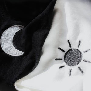 May include: A black and white fabric with a white crescent moon embroidered on the black side and a black sun embroidered on the white side.
