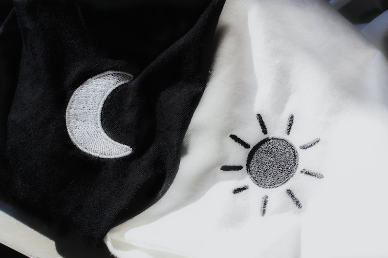 May include: A black and white fabric with a white crescent moon embroidered on the black side and a black sun embroidered on the white side.