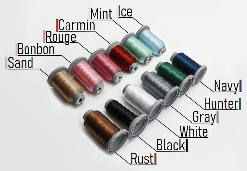 May include: A collection of 12 spools of thread in various colors, including sand, bonbon, carmin rouge, mint ice, rust, black, white, gray, hunter, navy, and two shades of brown. The spools are arranged in a diagonal line from top left to bottom right.