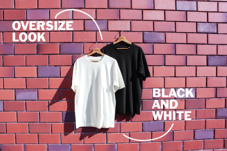 May include: Two oversized t-shirts hanging on hangers against a brick wall. The t-shirts are white and black. The text "OVERSIZE LOOK" is in the upper left corner of the image. The text "BLACK AND WHITE" is in the lower right corner of the image.