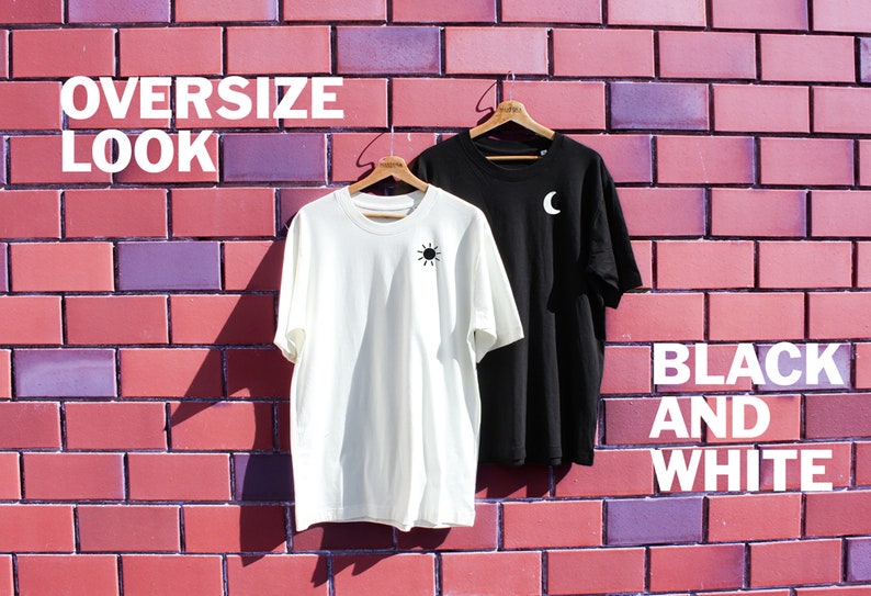 May include: Two oversized t-shirts hanging on wooden hangers against a brick wall. The t-shirt on the left is white with a black sun graphic. The t-shirt on the right is black with a white crescent moon graphic. The text "OVERSIZE LOOK" is at the top of the image and the text "BLACK AND WHITE" is at the bottom of the image.