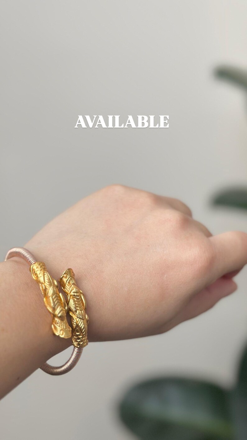 May include: Gold-colored bracelet with intricate, textured design. The bracelet is on a wrist, with the word "AVAILABLE" in white text in the background. The bracelet appears to be made of metal and has a detailed, ornate pattern.