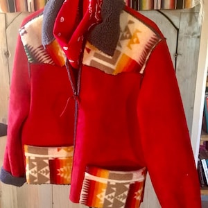 May include: A red fleece jacket with a southwestern patterned fleece lining on the collar, cuffs, and pockets. The jacket has a zipper closure and a red bandana tied around the collar.