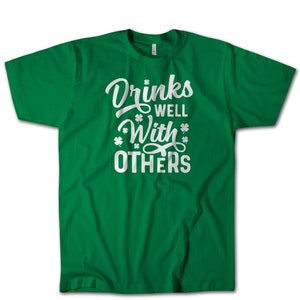 May include: Green t-shirt with white text that reads "Drinks Well With Others" and shamrock symbols.