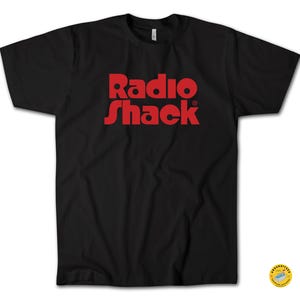 May include: Black t-shirt with the red text "Radio Shack" printed on the front. The text is in a bold, sans-serif font. The shirt is a crew neck style.