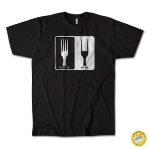 Puede incluir: Camiseta negra con un gráfico blanco. El gráfico presenta un tenedor y una mano haciendo el gesto de 'rock on', cada uno dentro de un rectángulo blanco. Debajo del tenedor está la palabra 'PLASTIC', y debajo de la mano 'METAL'.