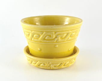 May include: A bright yellow ceramic planter with a matching saucer. The planter features a repeating geometric pattern around the rim and base. The pot is approximately 4 inches in diameter and 3 inches tall.