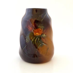 May include: A brown and orange ceramic vase with a floral design. The vase has a wavy, textured surface and features a bouquet of orange and yellow flowers with green leaves.