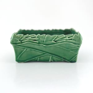 May include: A white ceramic mug with a black handle and the text "But First, Coffee" in a bold, black font. The mug is set against a blurred background, suggesting a cozy setting.