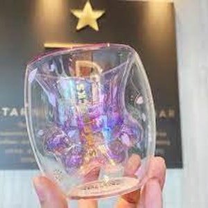 May include: A double-walled glass mug with a paw print design. The paw print is iridescent and has a purple and pink color scheme. The mug is clear glass with a pink rim.