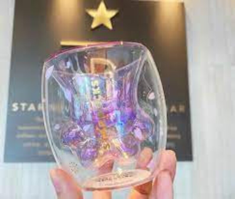 May include: A double-walled glass mug with a paw print design. The paw print is iridescent and has a purple and pink color scheme. The mug is clear glass with a pink rim.