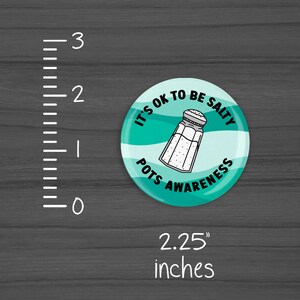 Puede incluir: Un bot&oacute;n redondo de 5,7 cm de di&aacute;metro con un fondo turquesa y texto blanco que dice "It's OK to be Salty Pots Awareness" con un contorno blanco de un salero en el centro.