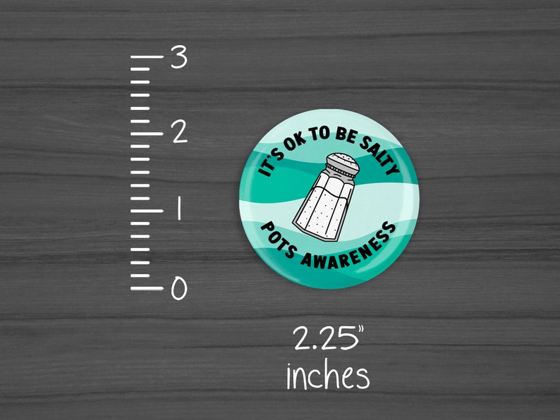 Puede incluir: Un bot&oacute;n redondo de 5,7 cm de di&aacute;metro con un fondo turquesa y texto blanco que dice "It's OK to be Salty Pots Awareness" con un contorno blanco de un salero en el centro.