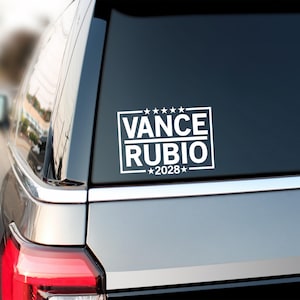 May include: White rectangular sticker with the text "VANCE RUBIO 2028" in a bold, sans-serif font. The sticker is on the rear window of a vehicle. The text is enclosed in a white rectangular border with five stars above the name.