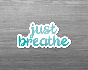 May include: A white sticker with the words "just breathe" in a teal script font. The sticker has a white border and is set against a gray wood grain background.