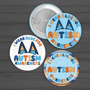 May include: Three round buttons with the text "I WEAR BLUE FOR AUTISM AWARENESS". The buttons are blue, orange, and white. One button has a paw print design, and the others have a stylized AA symbol.