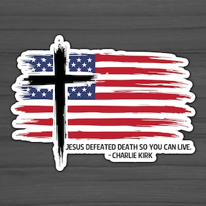May include: A sticker featuring a stylized American flag design with a black cross overlay. The flag has red and white stripes and a blue field with white stars. The text reads: "JESUS DEFEATED DEATH SO YOU CAN LIVE. - CHARLIE KIRK."