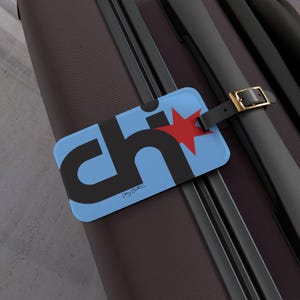 May include: Blue luggage tag with a black and red "CHI" logo and a red star. The tag is attached to a black suitcase with a gold buckle.